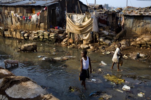 A boy walks through the river in Kroo Bay slum looking for scrap metal to sell. The river is effectively a giant sewage and everyday new garbage arrives in the water from the hills around. Kroo Bay, Freetown, Sierra Leone.